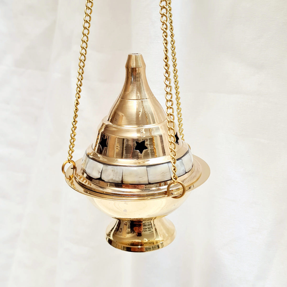 Hanging brass incense burner with mother-of-pearl bands, a pointed lid, star-shaped vents and three chains.