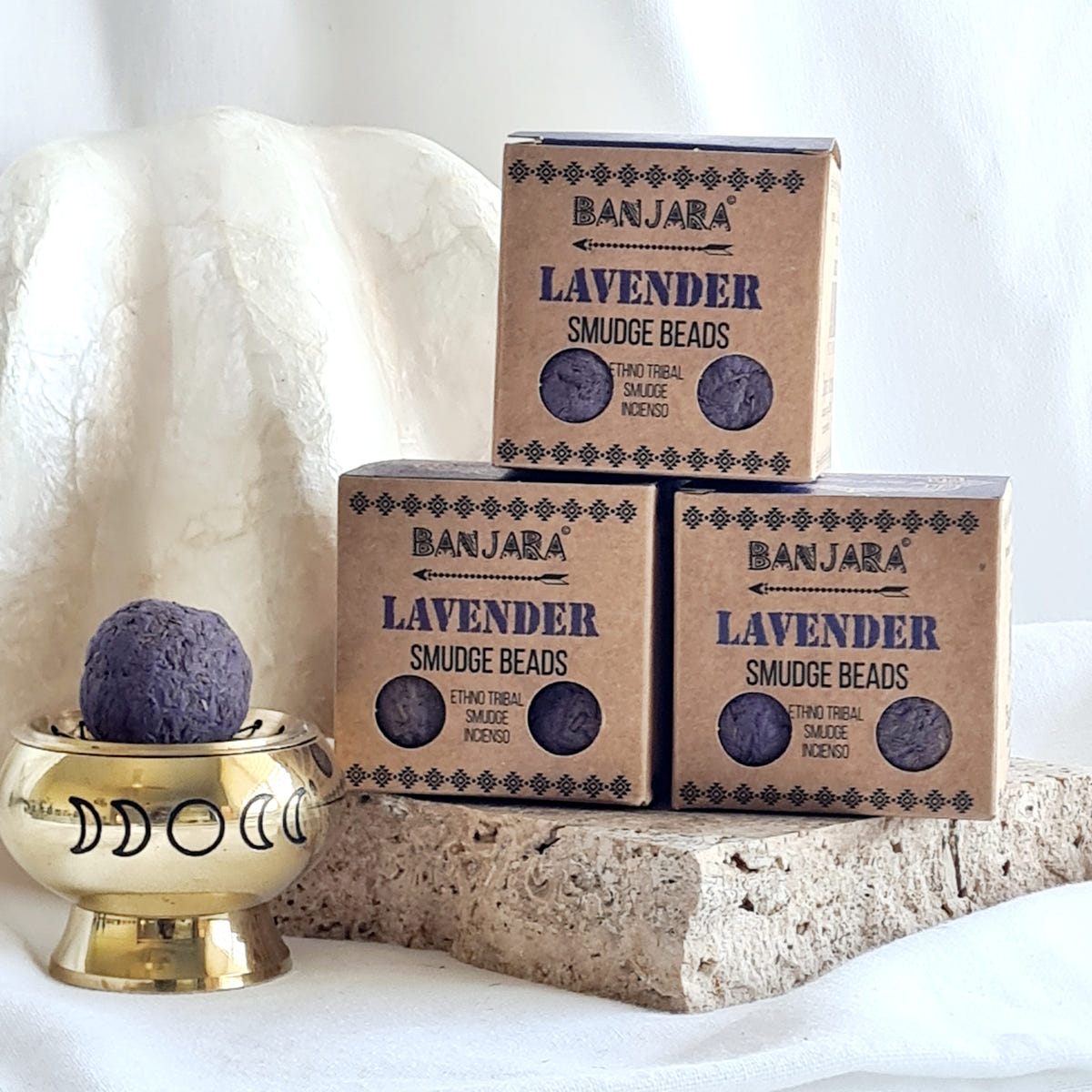 Three Banjara Lavender smudge bead boxes beside a brass moon-design burner holding a purple round bead.