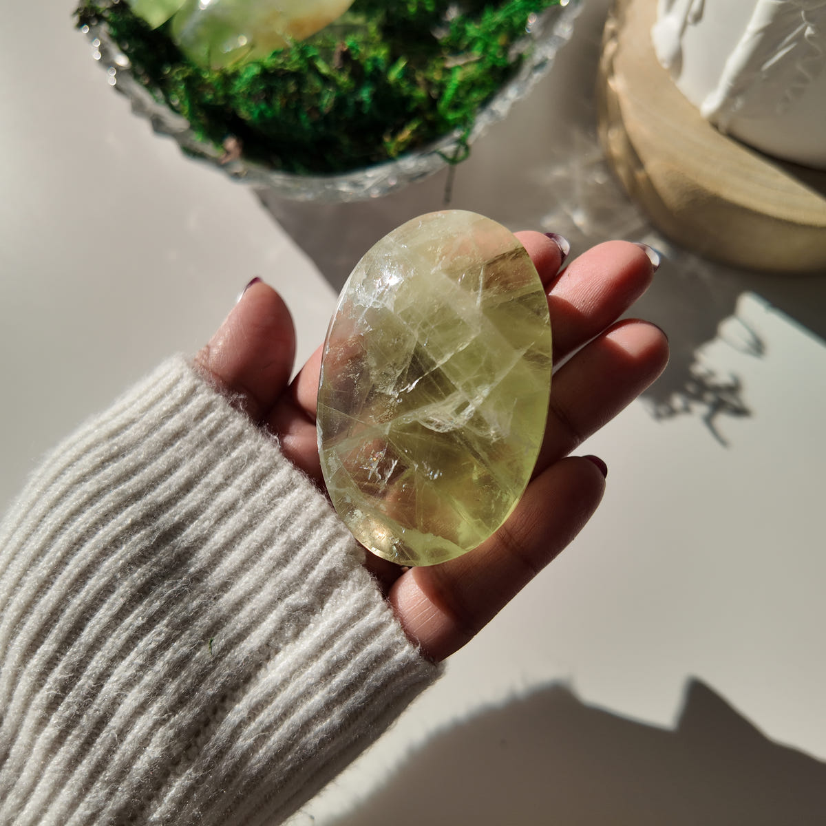 Hand holding polished pale-green Fluorite pocket stone M, with translucent areas and internal veils.