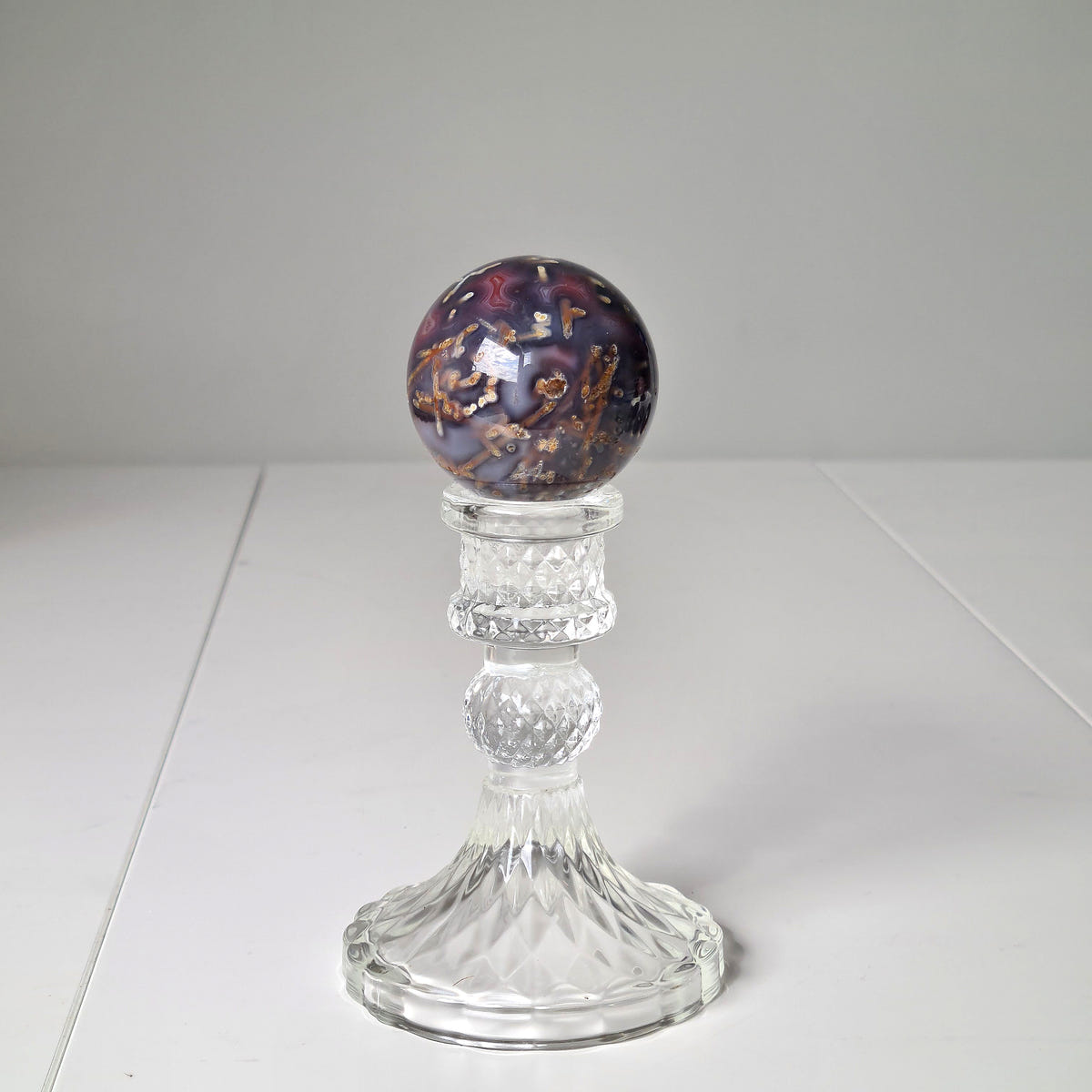Swazi agate sphere F with dark red, purple and golden mottling on a tall clear decorative stand.