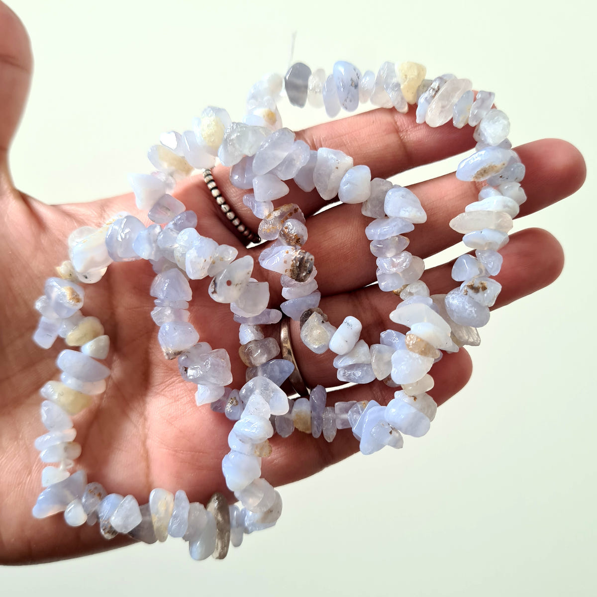 Pale blue lace agate chip bracelets with irregular translucent beads held in a hand.