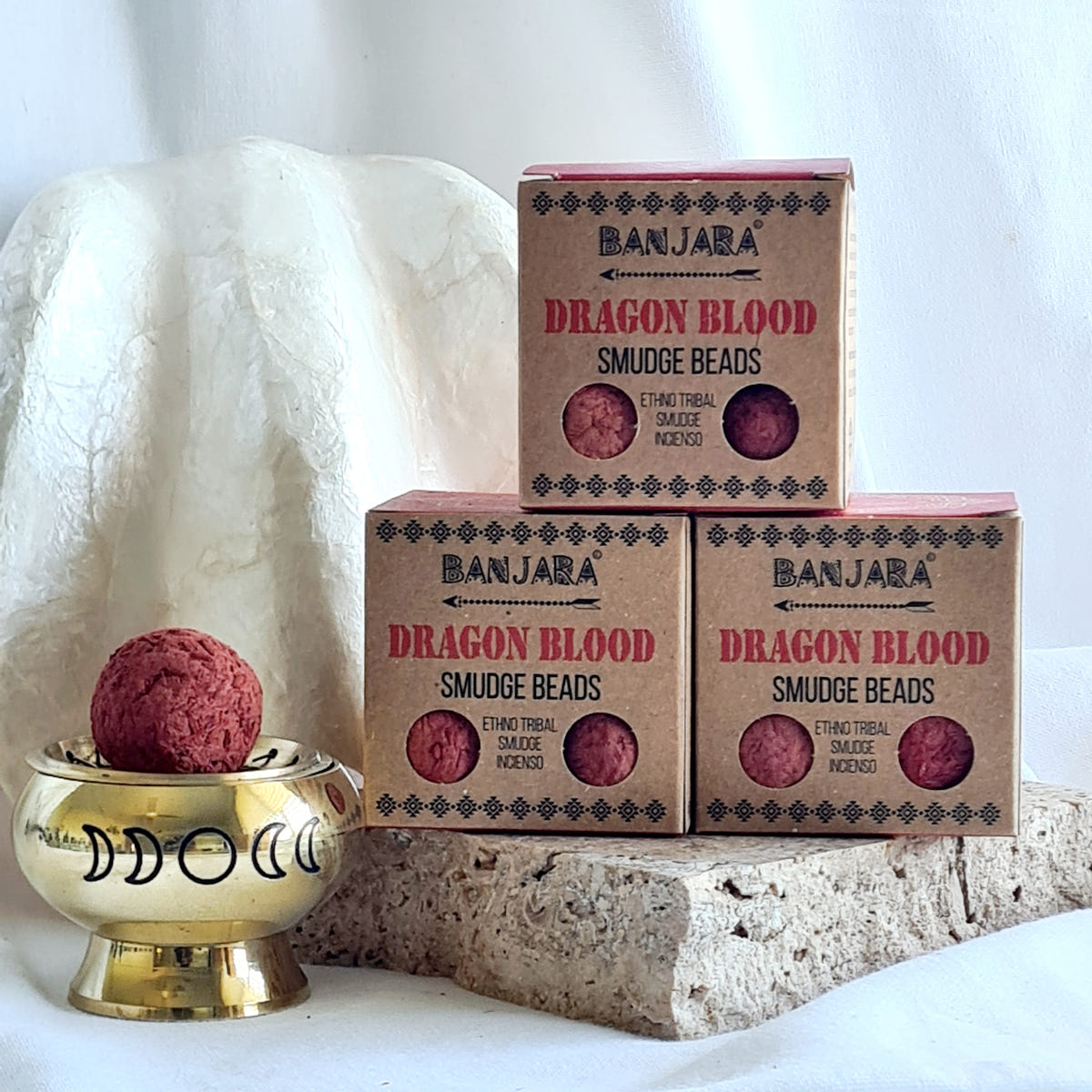 Three Banjara Dragon Blood smudge bead boxes beside a brass burner holding a red round bead.