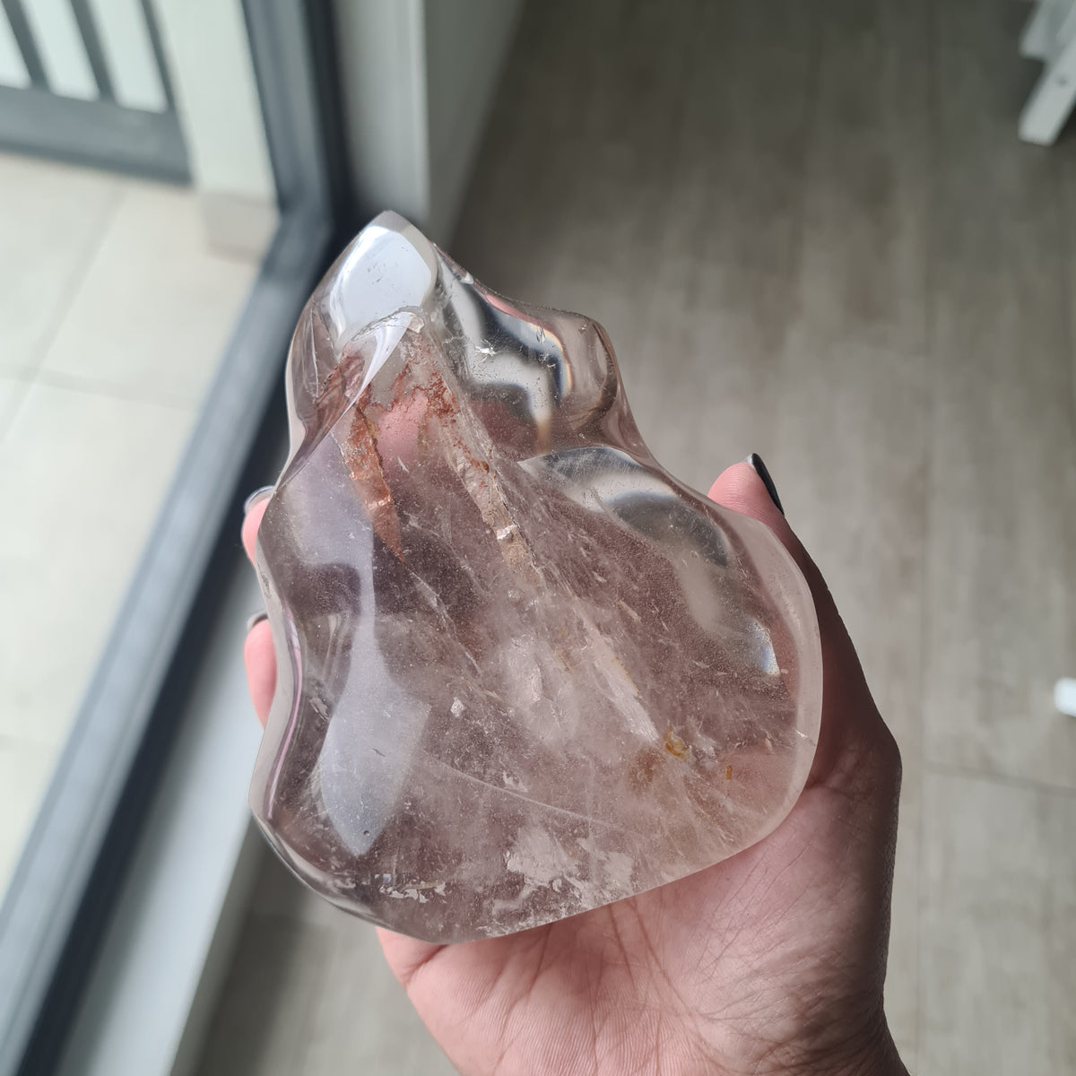 Hand holding a polished quartz flame with smoky tones and natural inclusions.