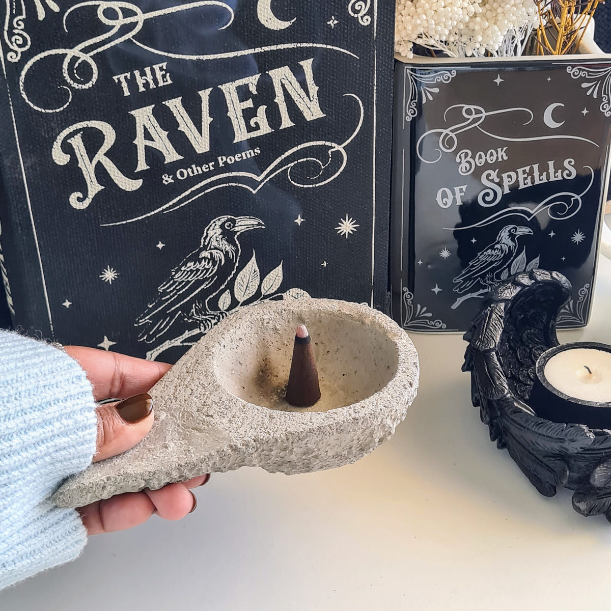 Hand holding a textured stone incense burner with a round recessed bowl and an incense cone at its centre.
