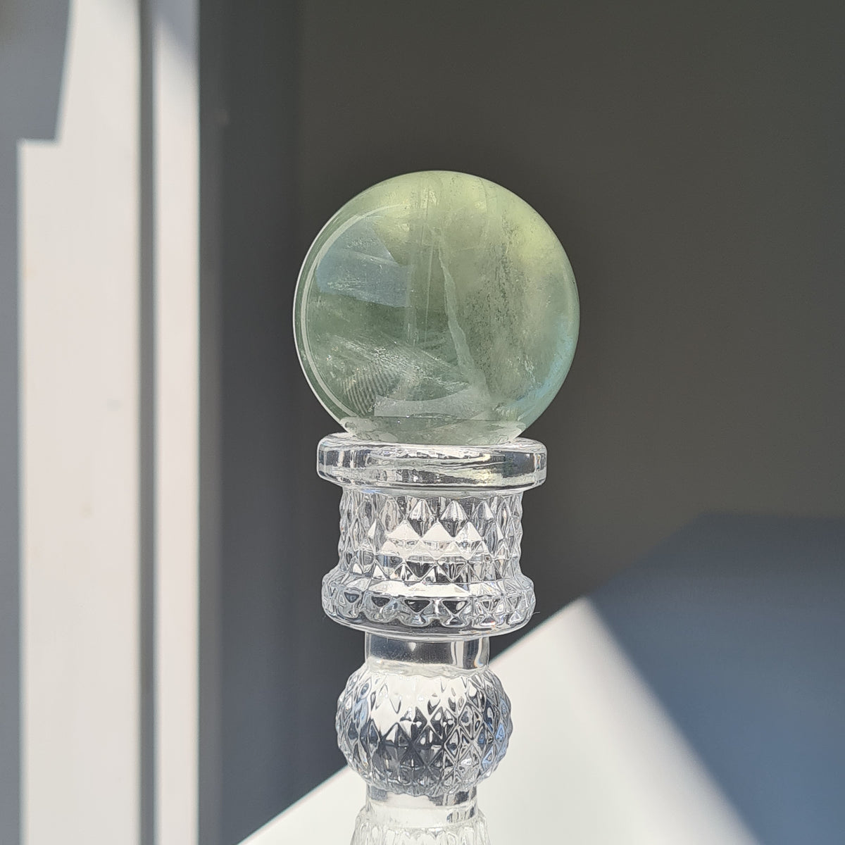 Pale green fluorite sphere with fine natural bands on a clear decorative stand.