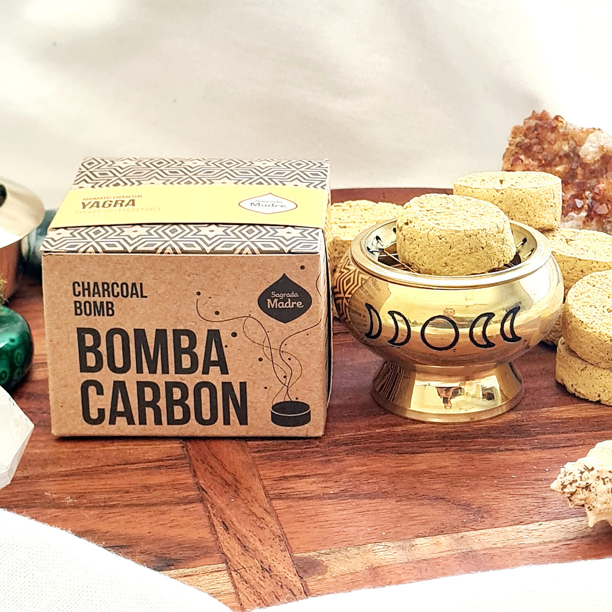 Sagrada Madre Yagra Bomba Carbon box beside yellow incense charcoal pieces and a brass moon-design burner.