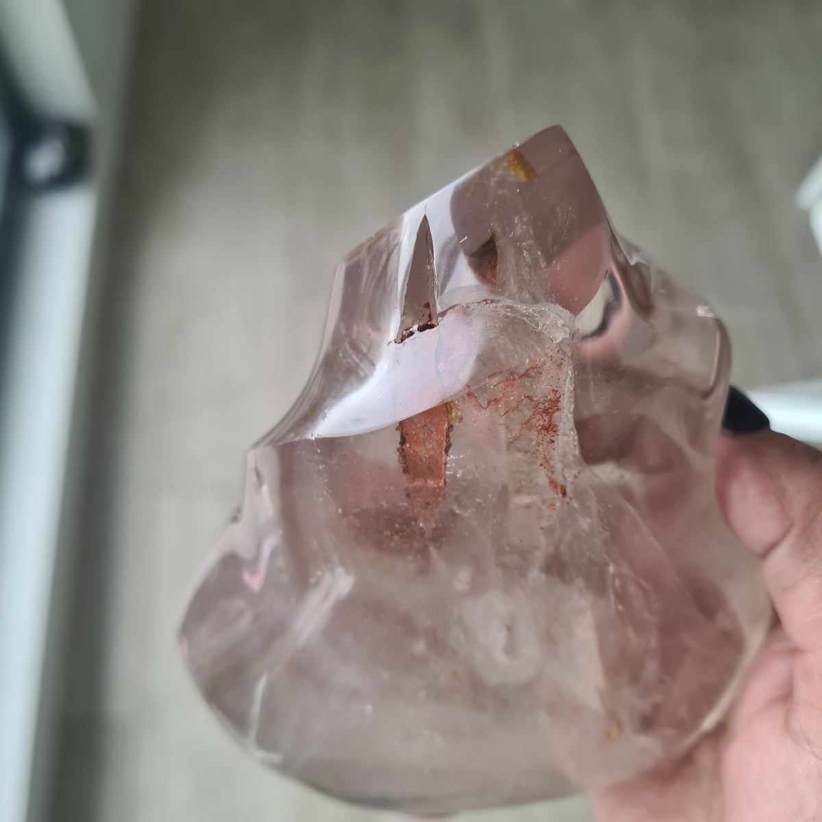 Hand holding a polished quartz flame with smoky tones and natural inclusions.