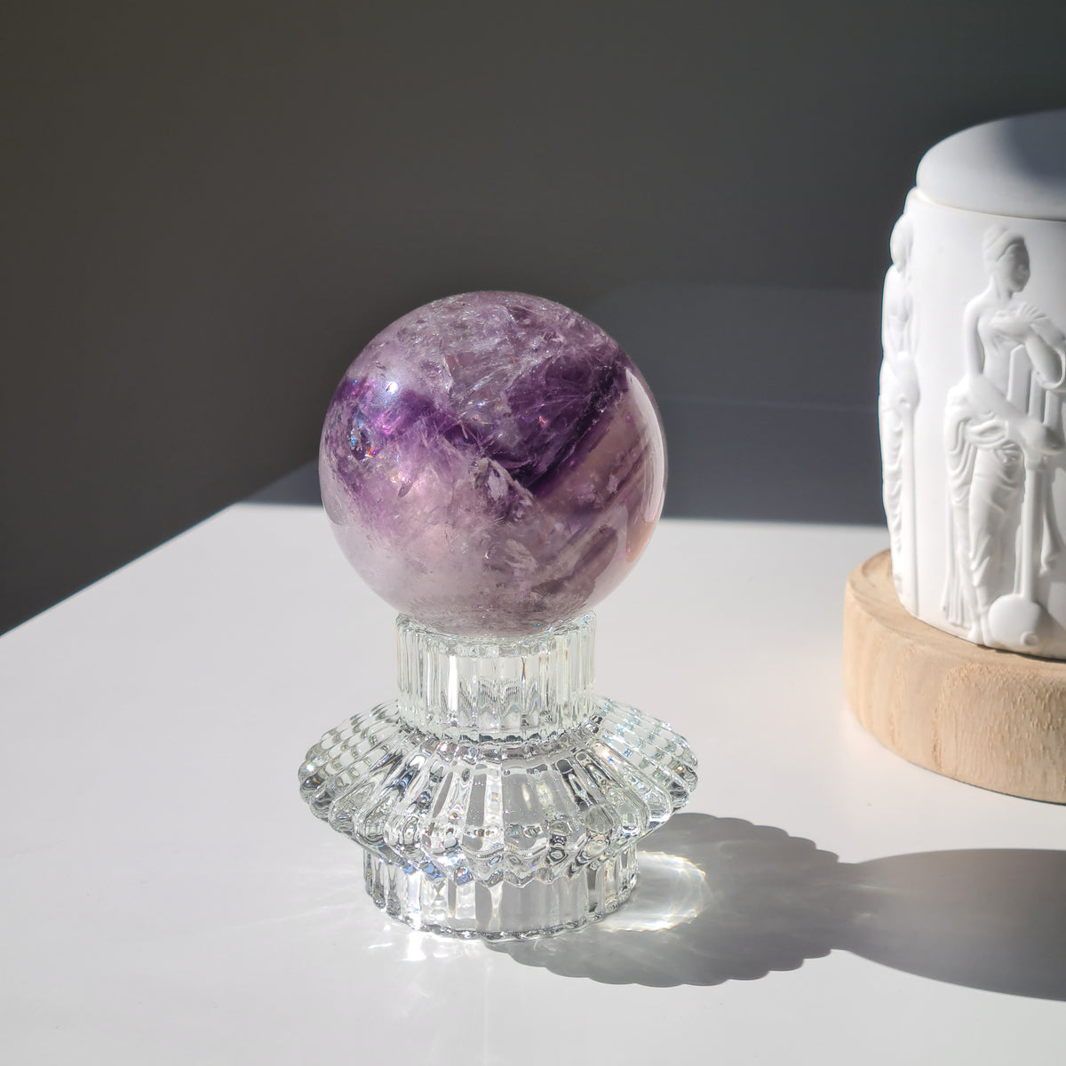 Amethyst phantom sphere with purple bands and pale inclusions on a clear decorative stand.