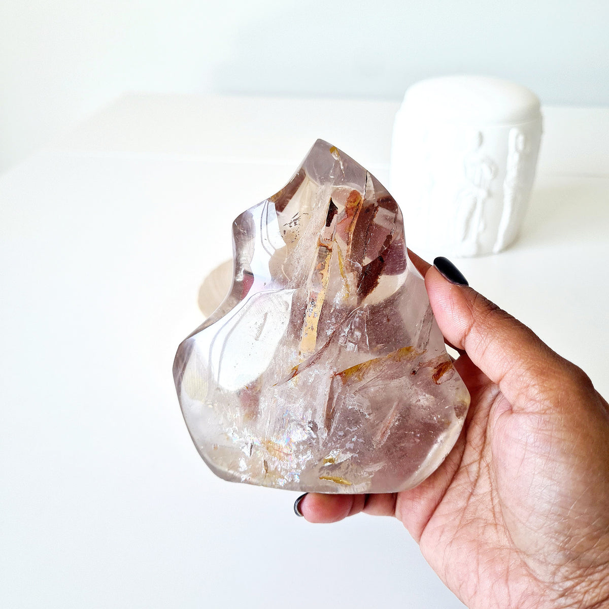 Hand holding a polished quartz flame with smoky tones and golden-brown inclusions.