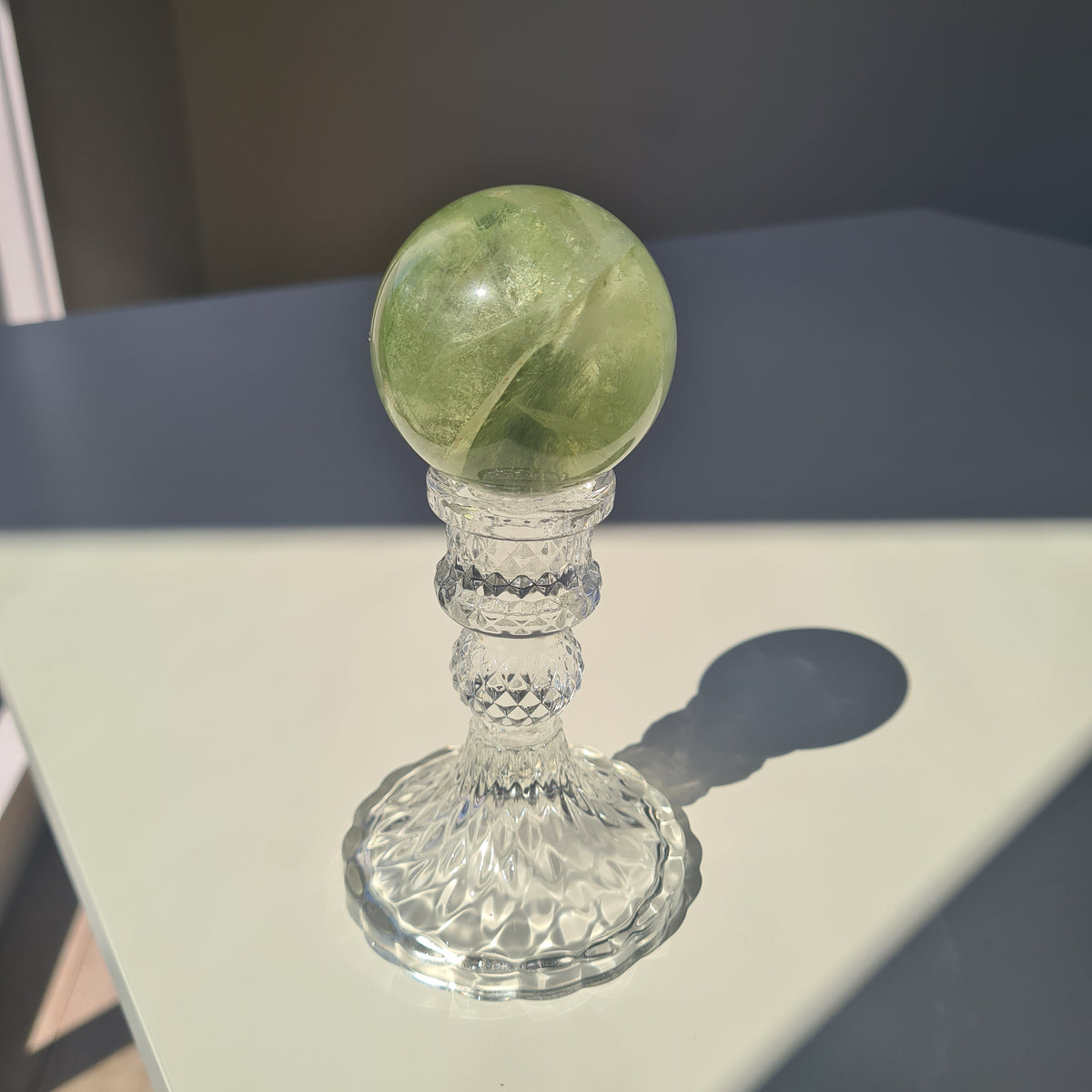 Golden-green fluorite sphere with translucent layers on a clear decorative stand.