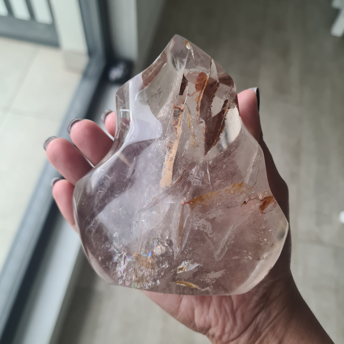 Hand holding a polished quartz flame with smoky tones and natural inclusions.