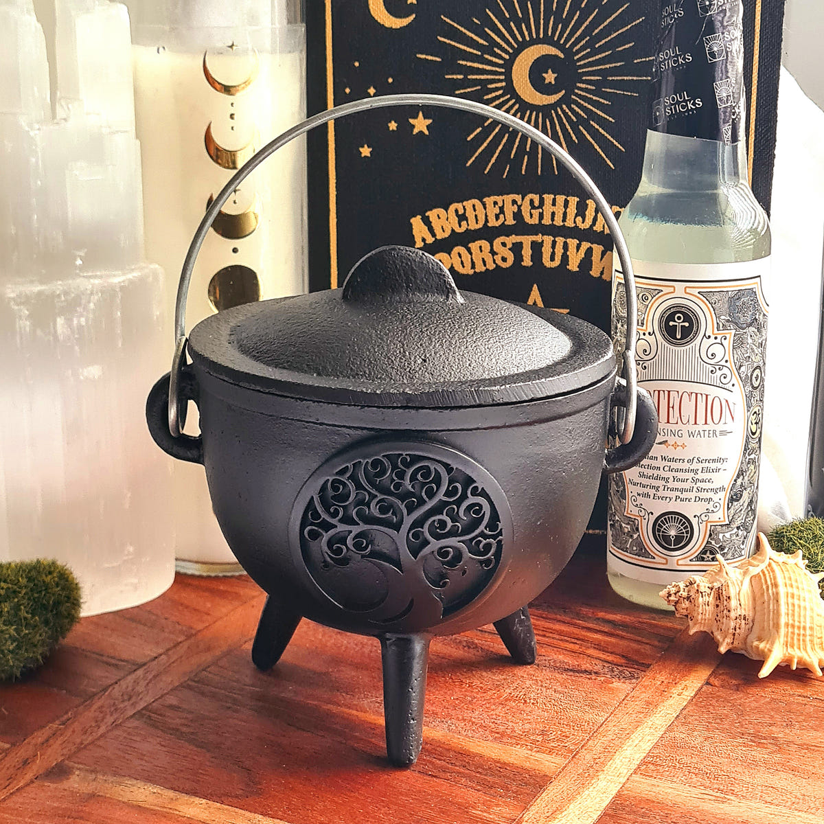 Black cast iron cauldron with a Tree of Life motif, fitted lid, curved handle and three legs.