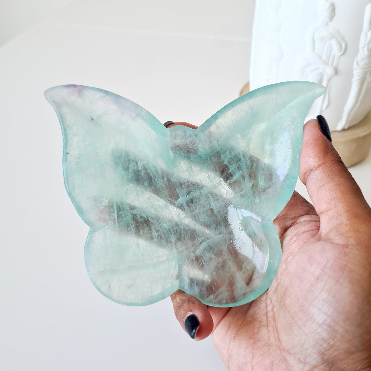 Hand holding fluorite butterfly bowl 01 with pale mint-green wings and cloudy white veils.