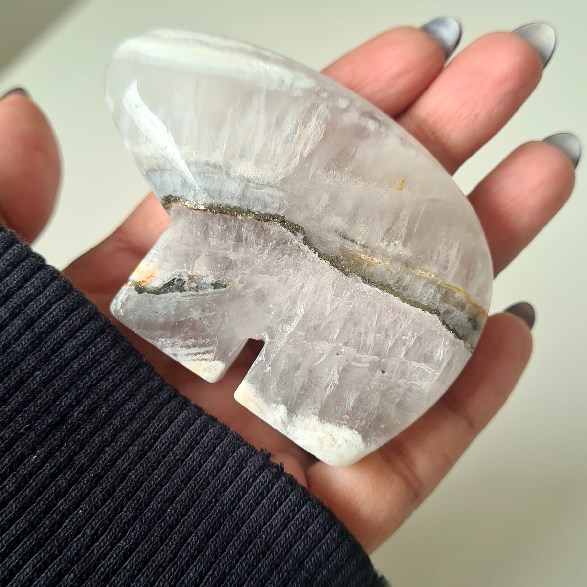 Hand holding a quartz and pyrite Zuni bear carving with a translucent pale body and a narrow metallic seam.