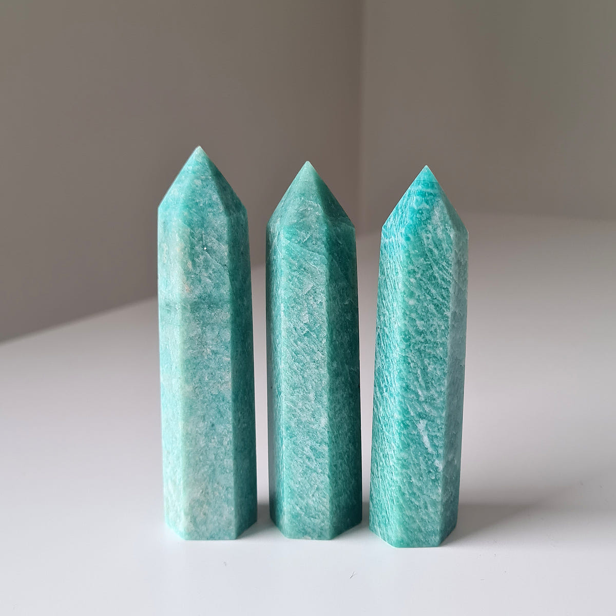 Three blue-green Amazonite crystal points standing upright on a pale surface.