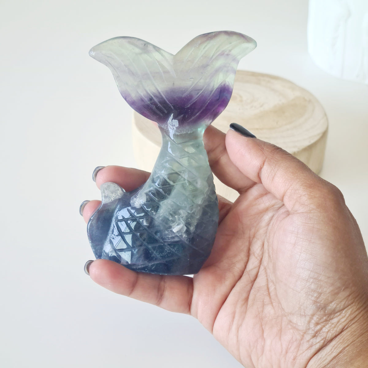 Hand holding a fluorite mermaid tail carving with purple bands and a blue-green base.