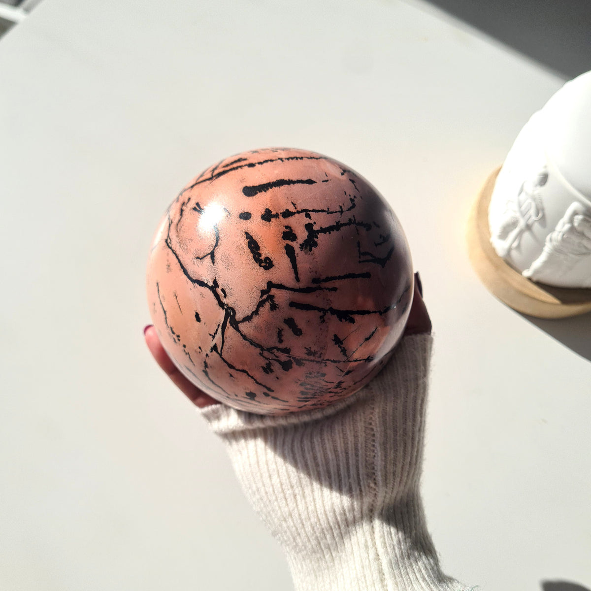 Picture jasper sphere held in one hand, showing scattered black markings on a peach surface.