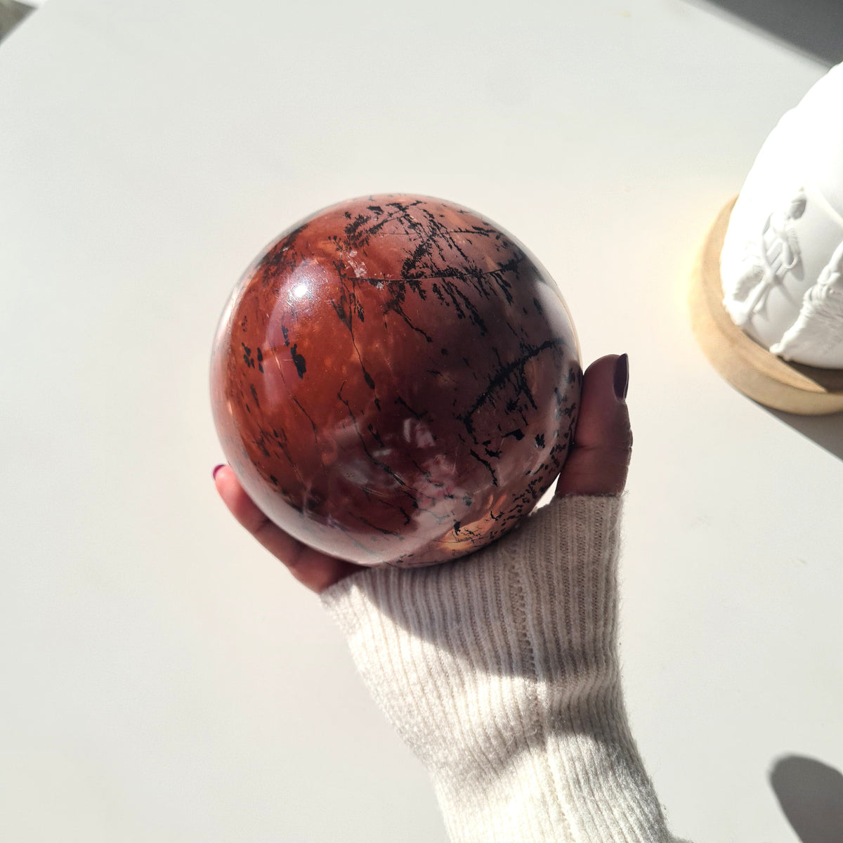Picture jasper sphere held in sunlight, showing a deep red face with black markings and pale patches.