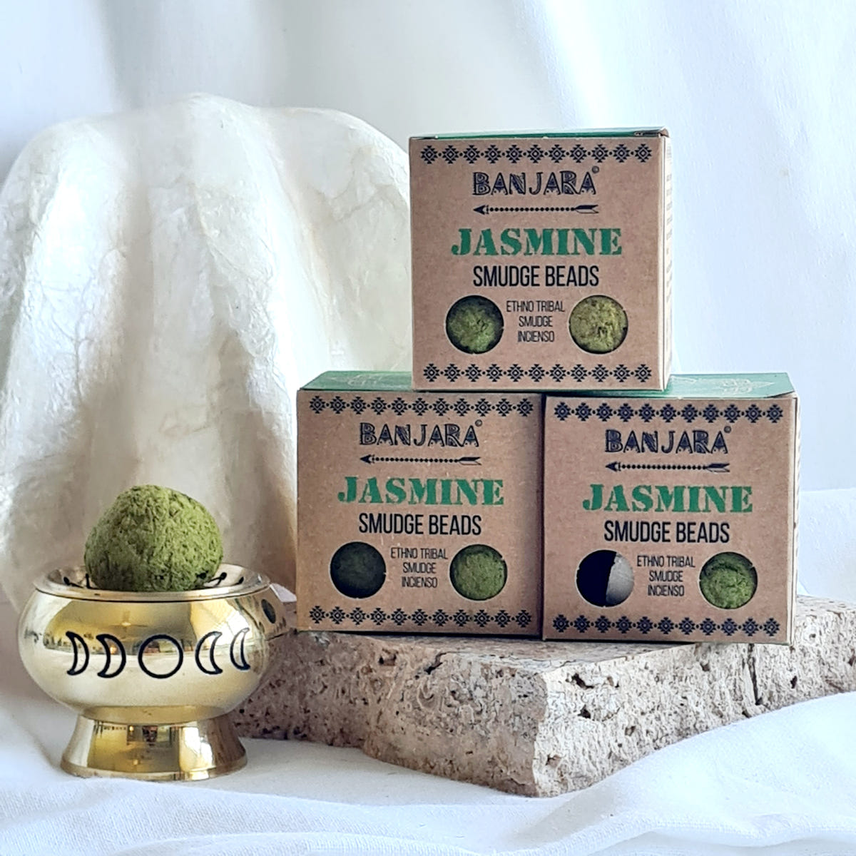 Three Banjara Jasmine smudge bead boxes beside a brass moon-design burner holding a green round bead.