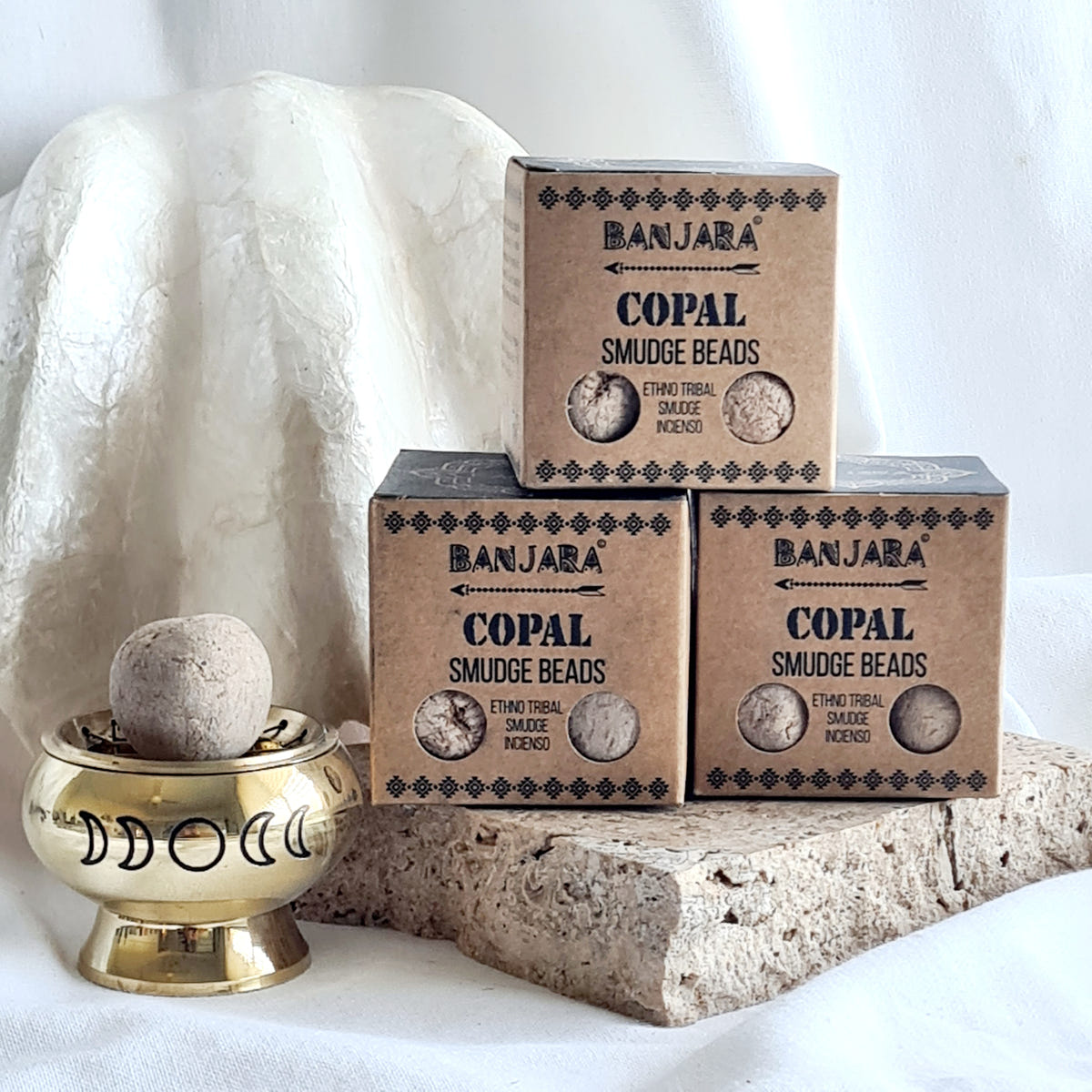 Three Banjara Copal smudge bead boxes beside a brass moon-design burner holding a round bead.
