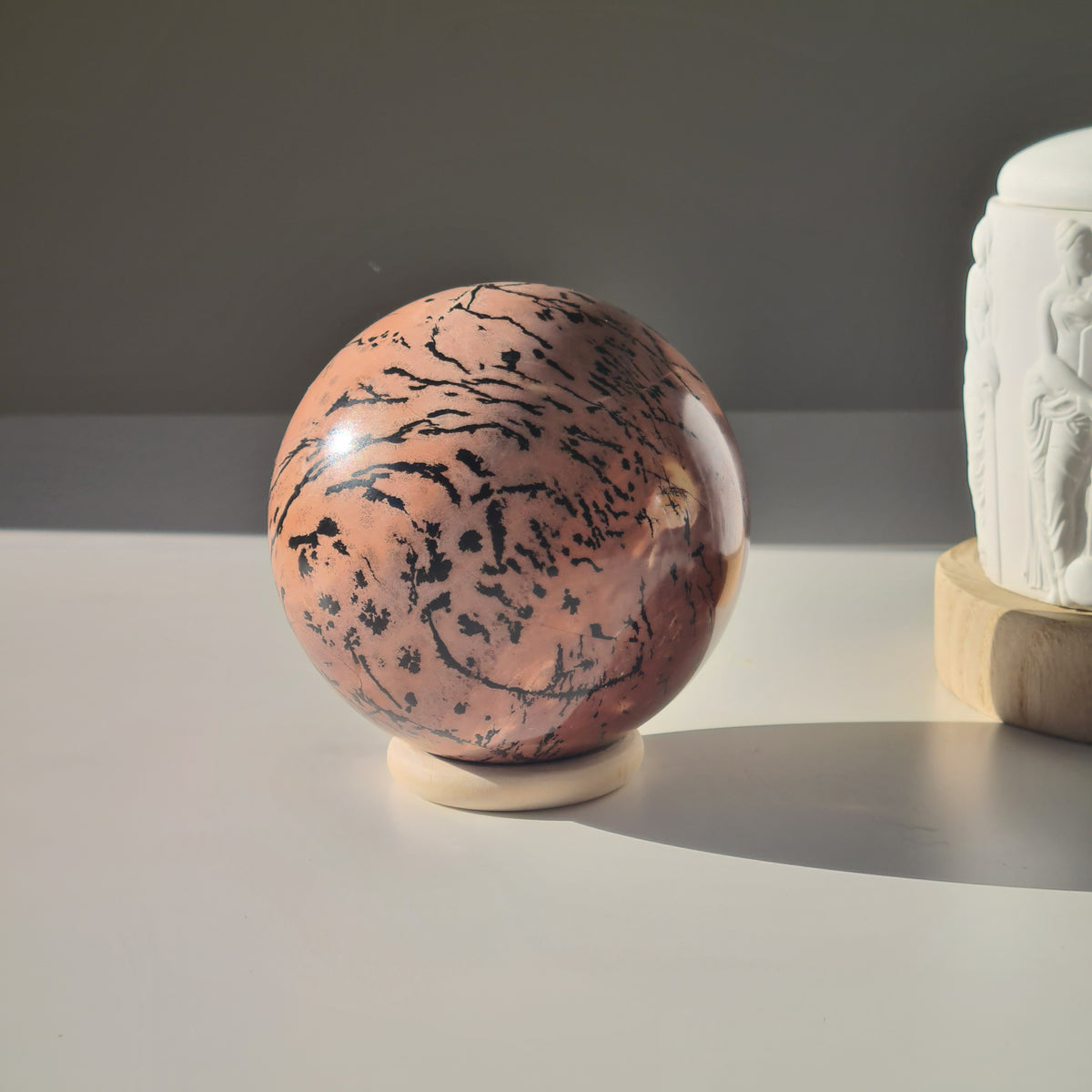 Picture jasper sphere on a pale ring stand, showing peach tones and fine branching black markings.