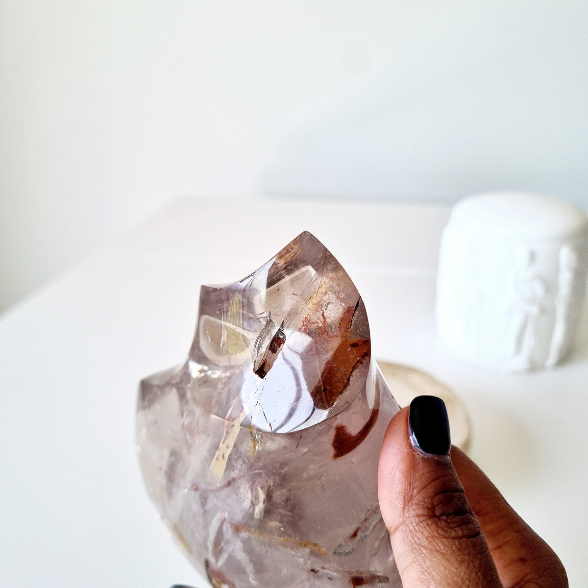 Hand holding a polished quartz flame with smoky tones and golden-brown inclusions.