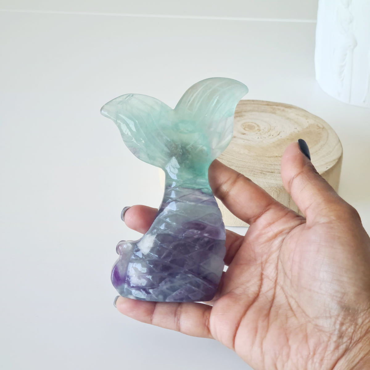 Hand holding a pale green and purple fluorite mermaid tail carving.