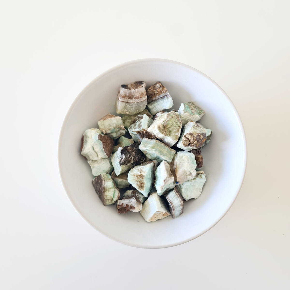 Tiny rough hemimorphite pieces with pale green and cream faces and brown edges arranged in a white bowl.