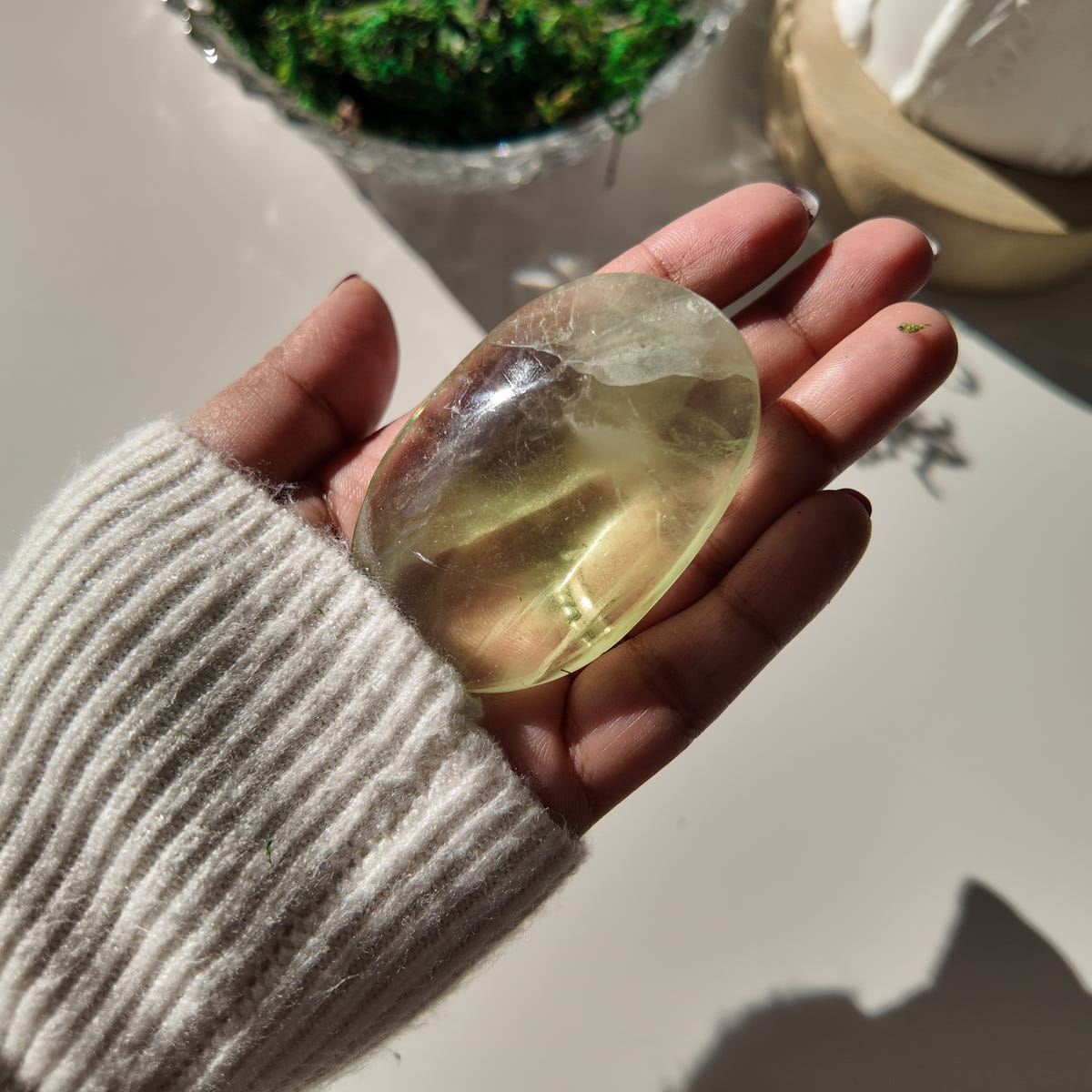 Hand holding polished pale-green Fluorite pocket stone O, with translucent areas and internal veils.