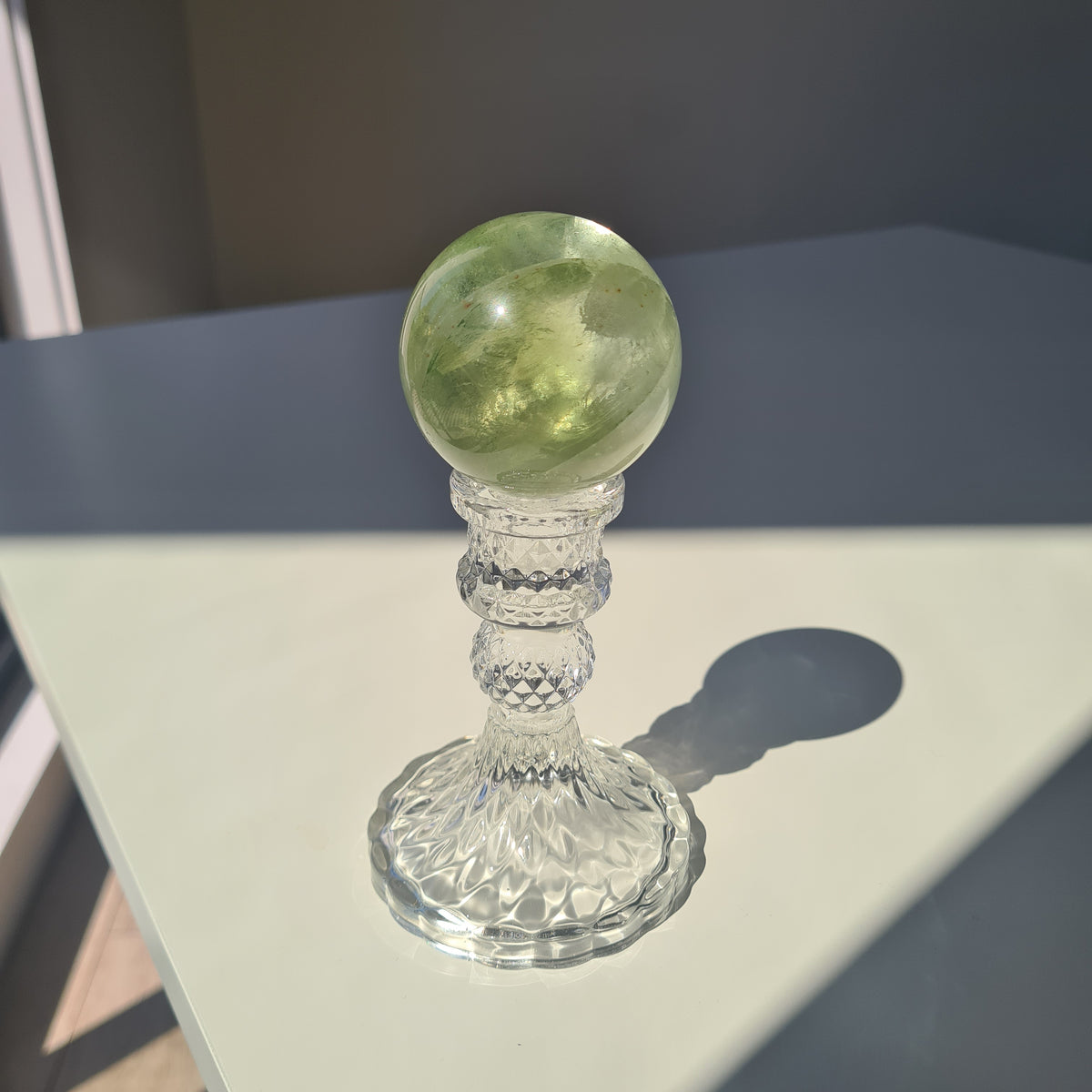 Golden-green fluorite sphere with translucent layers on a clear decorative stand.