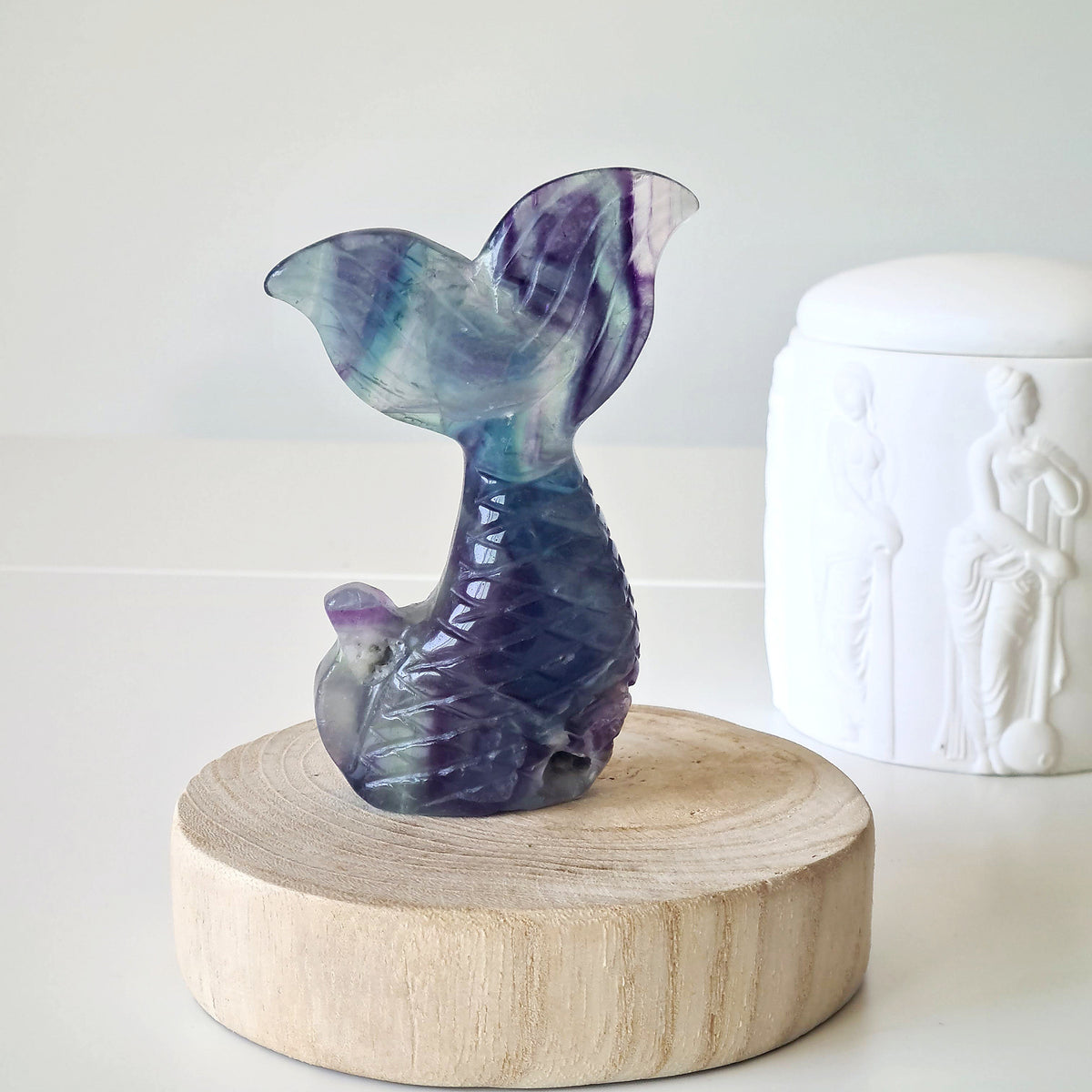 Purple and green fluorite mermaid tail carving on a round wooden display.
