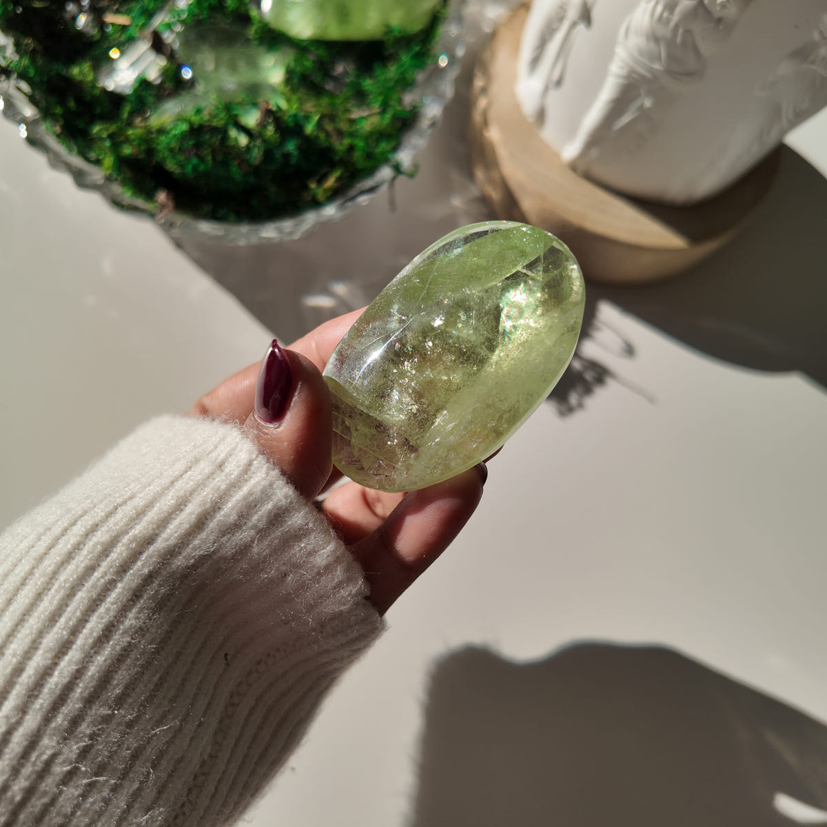 Hand holding polished pale-green Fluorite pocket stone Q, with translucent areas and internal veils.