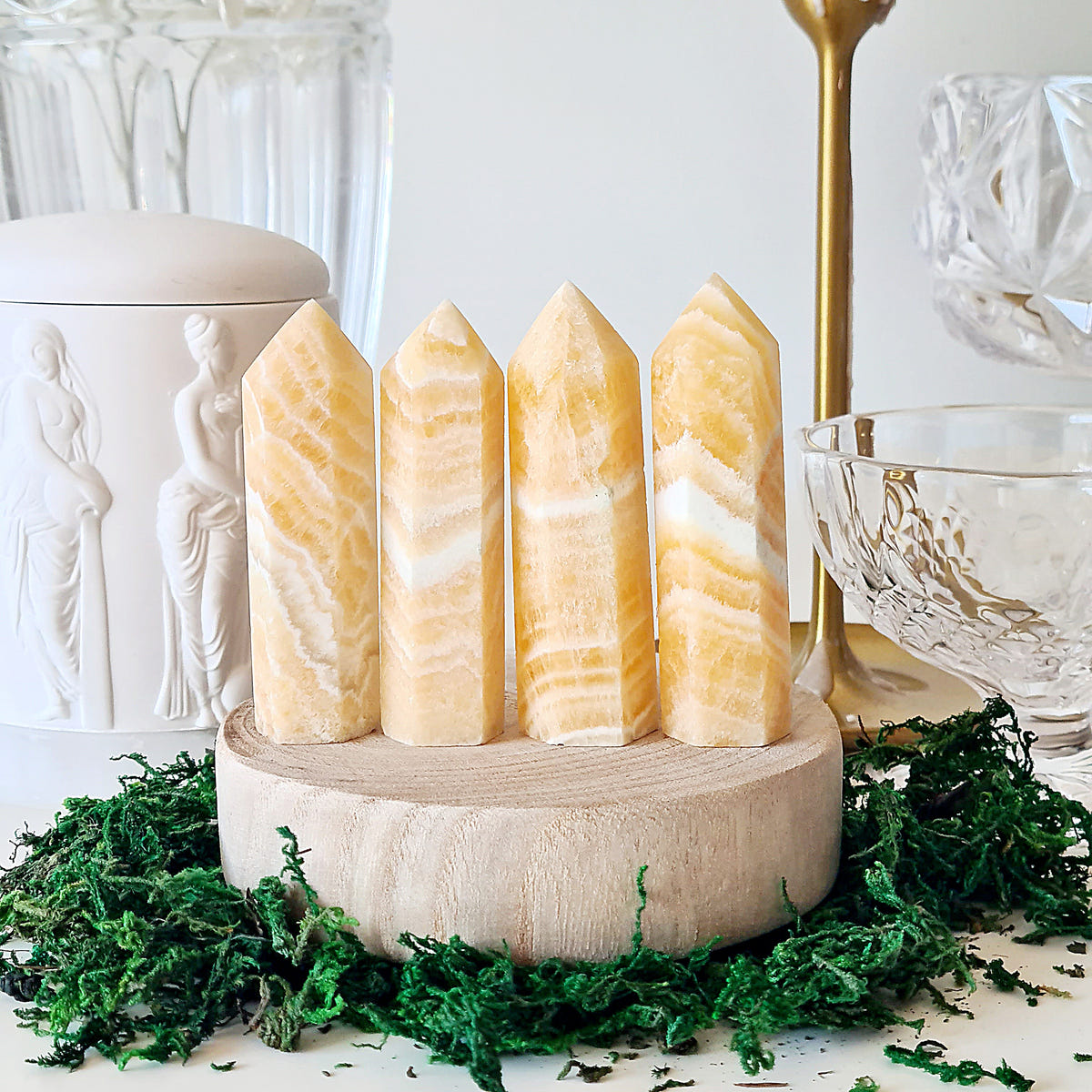 Four orange calcite points with cream and golden bands displayed on a round wooden base.