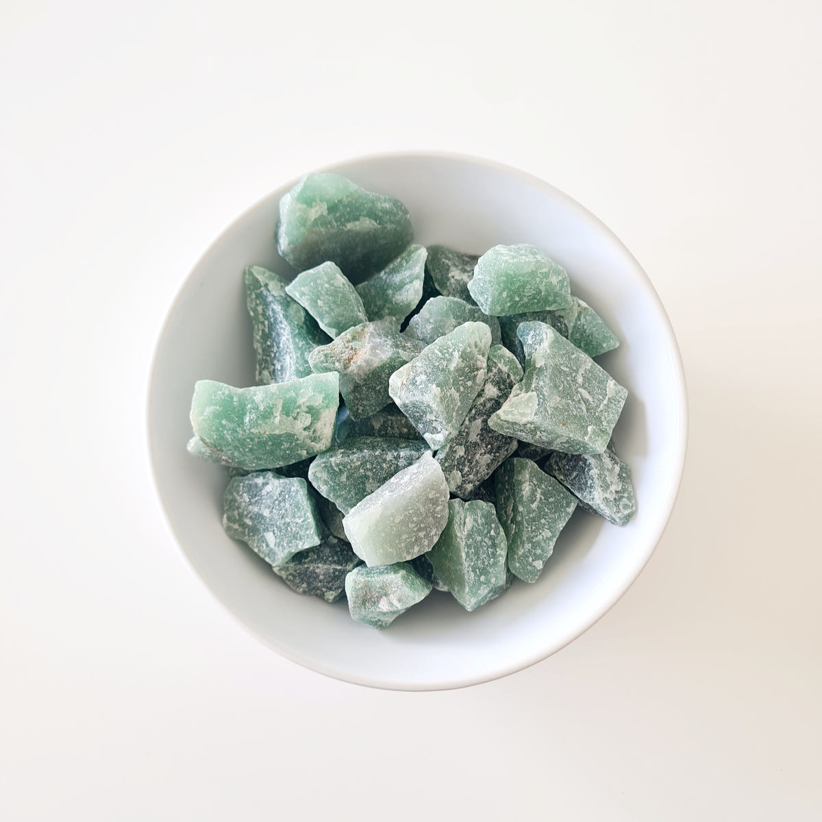 Small rough green aventurine stones with angular pale green surfaces arranged in a white bowl.