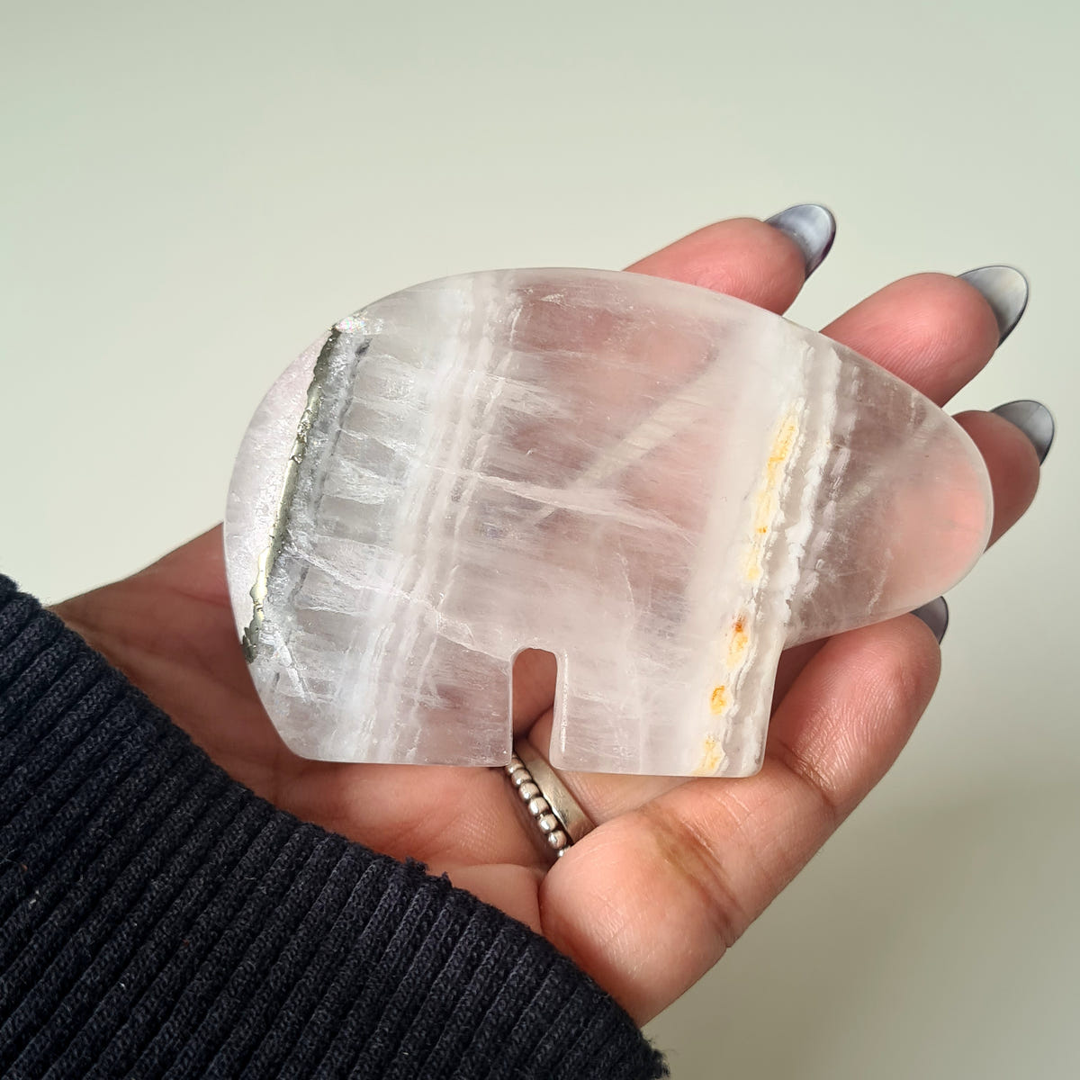 Hand holding a quartz and pyrite Zuni bear carving with pale pink and white bands and a fine golden stripe.