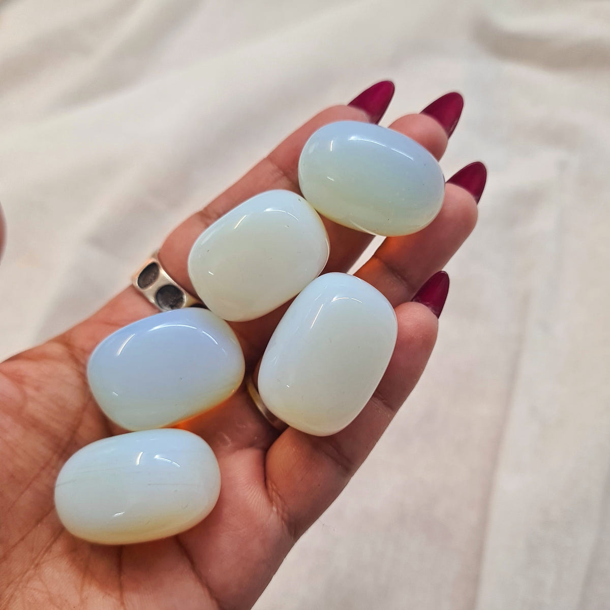 Hand holding smooth man-made opalite tumbles with milky blue surfaces and warm golden edges.