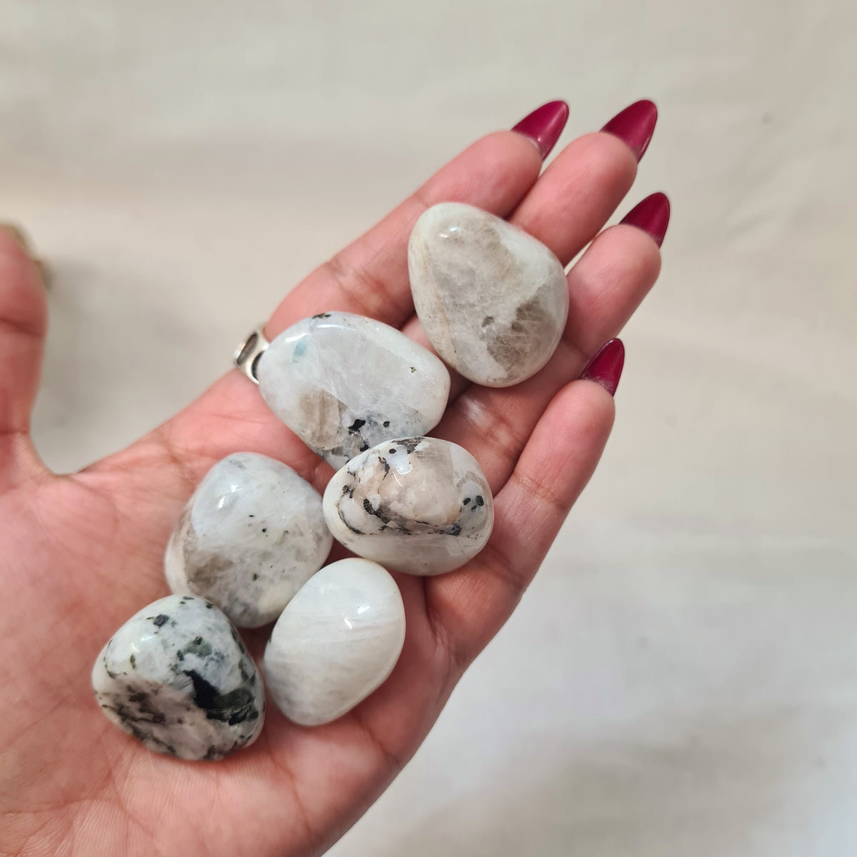 Hand holding smooth moonstone tumbles in white and pale grey with dark mineral inclusions.