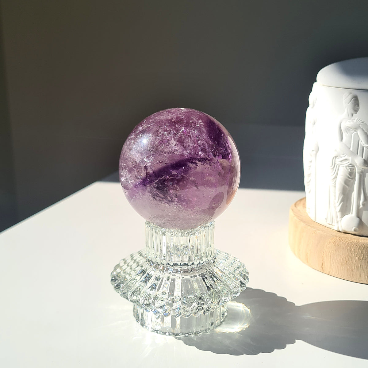 Amethyst phantom sphere with purple bands and pale inclusions on a clear decorative stand.