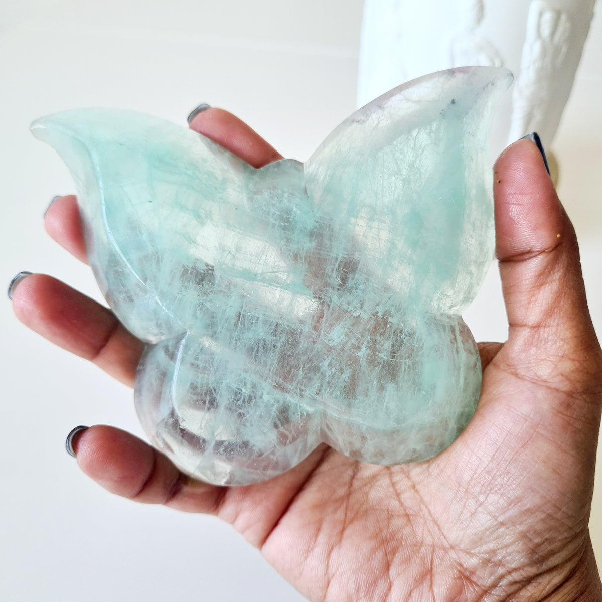 Hand holding a pale mint-green fluorite butterfly bowl with white natural patterns.