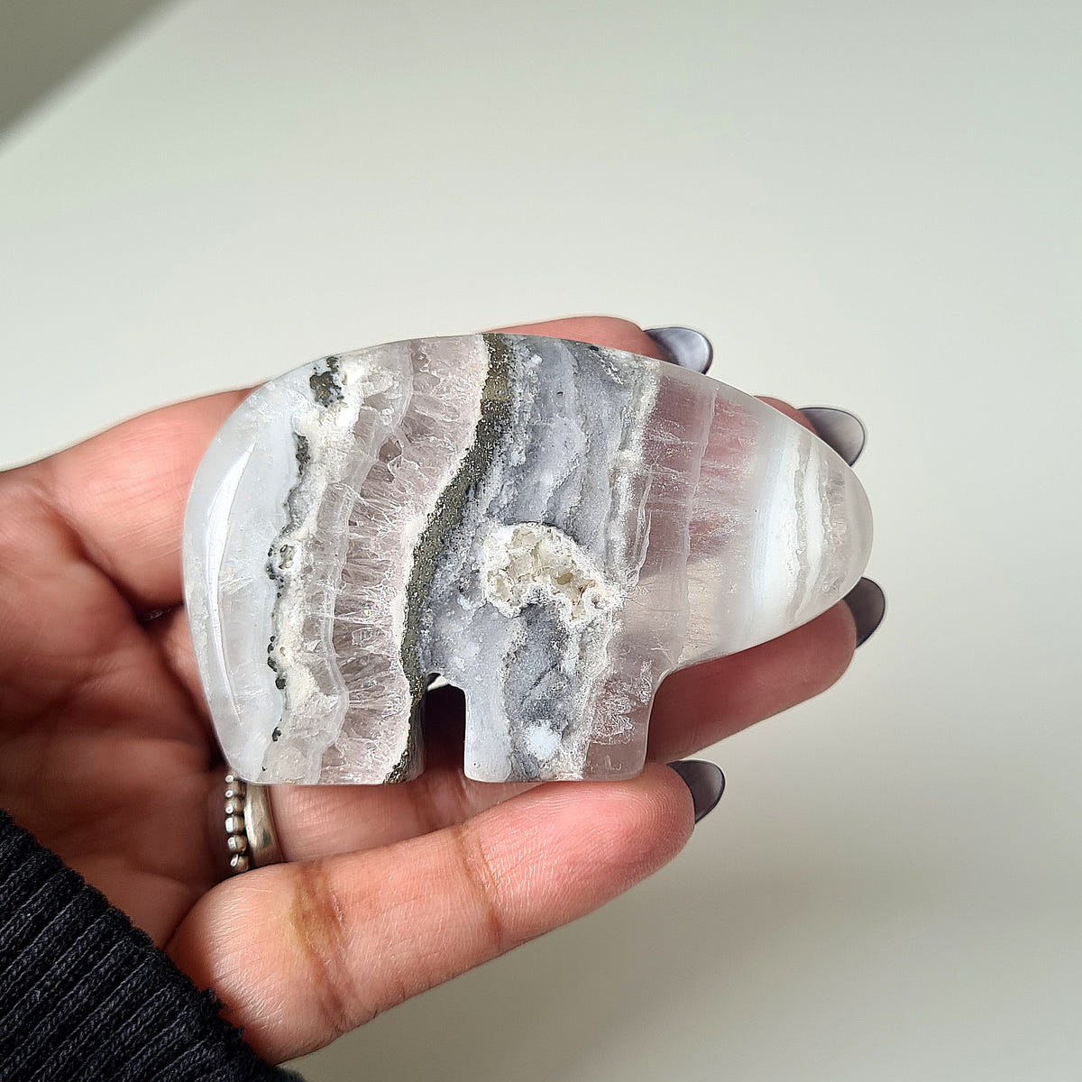 Hand holding a Quartz bear carving with grey and white bands and a textured crystal centre.