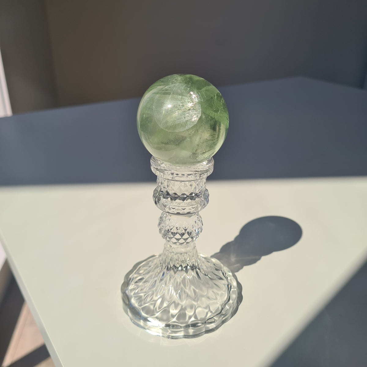 Green fluorite sphere with pale natural bands on a clear decorative stand in sunlight.