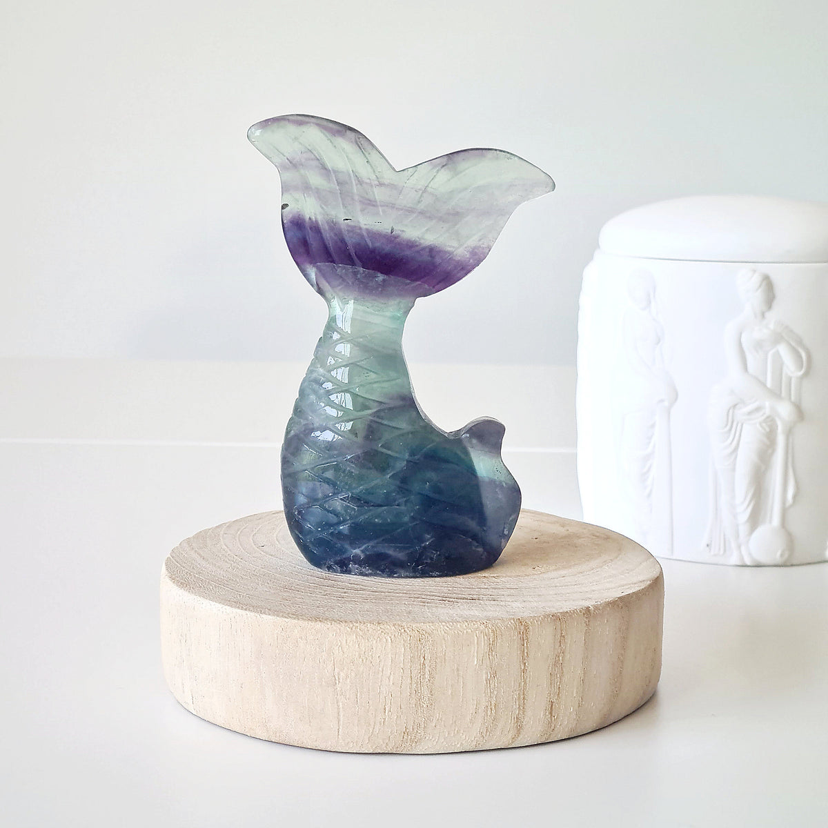 Fluorite mermaid tail carving with purple bands and a blue-green base on a wooden display.