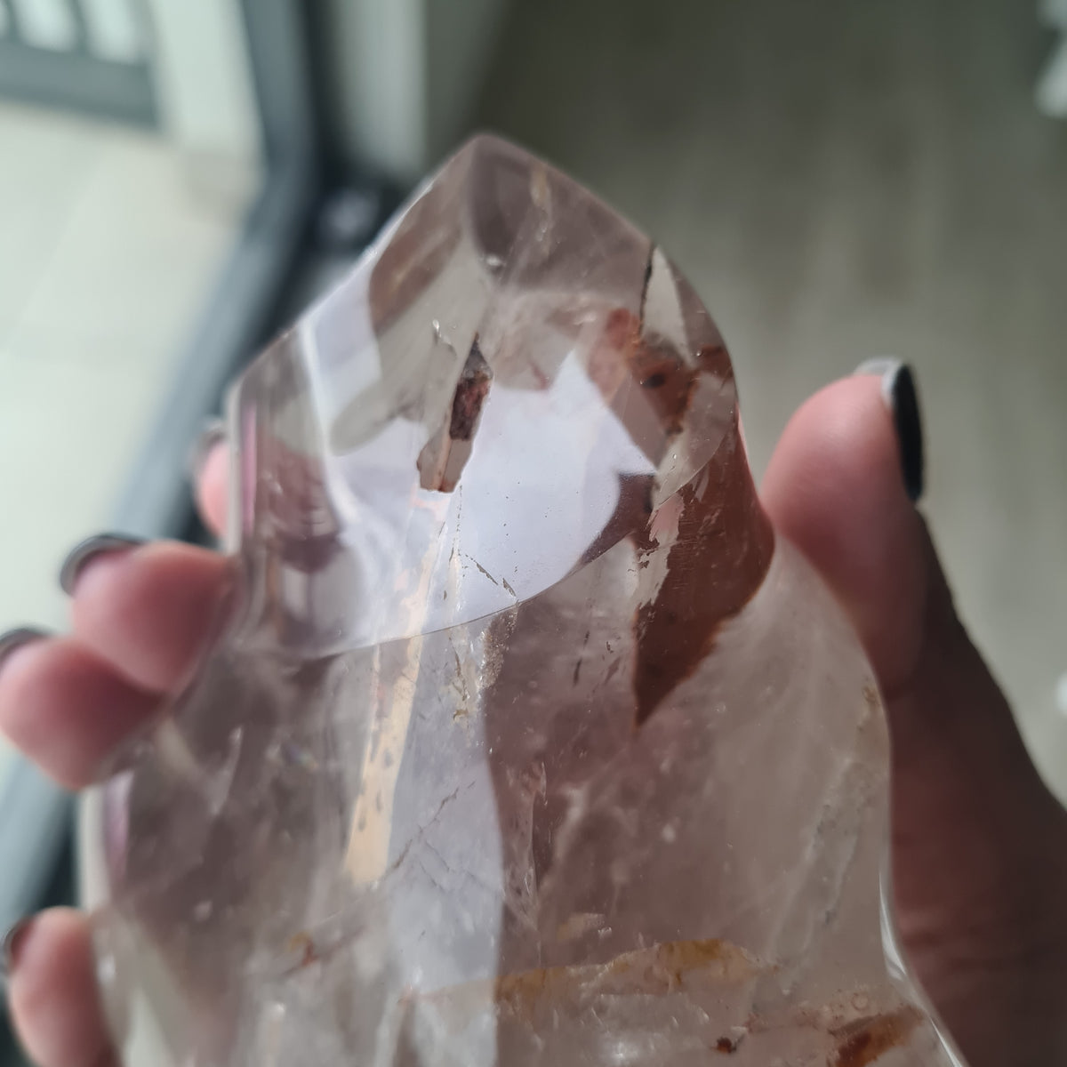 Hand holding a polished quartz flame with smoky tones and natural inclusions.
