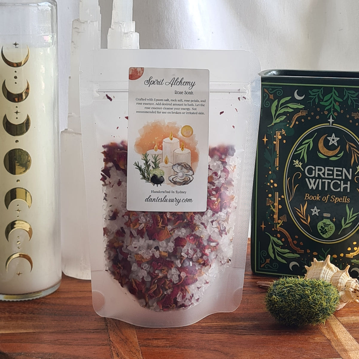 Spirit Alchemy soak pouch showing pink and white crystals and dried flower petals beside a green illustrated book.