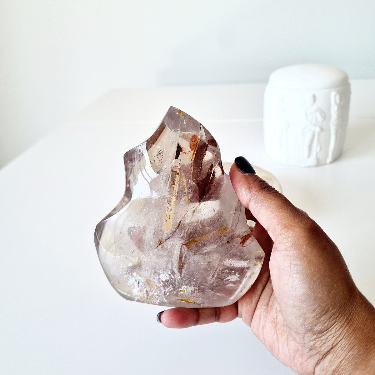 Hand holding a polished quartz flame with smoky tones and golden-brown inclusions.