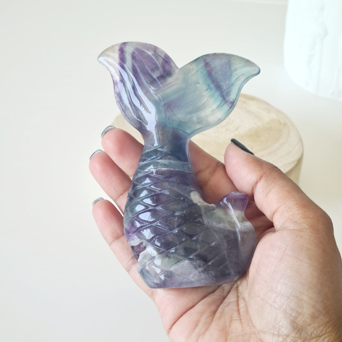 Hand holding a purple and green fluorite mermaid tail carving.
