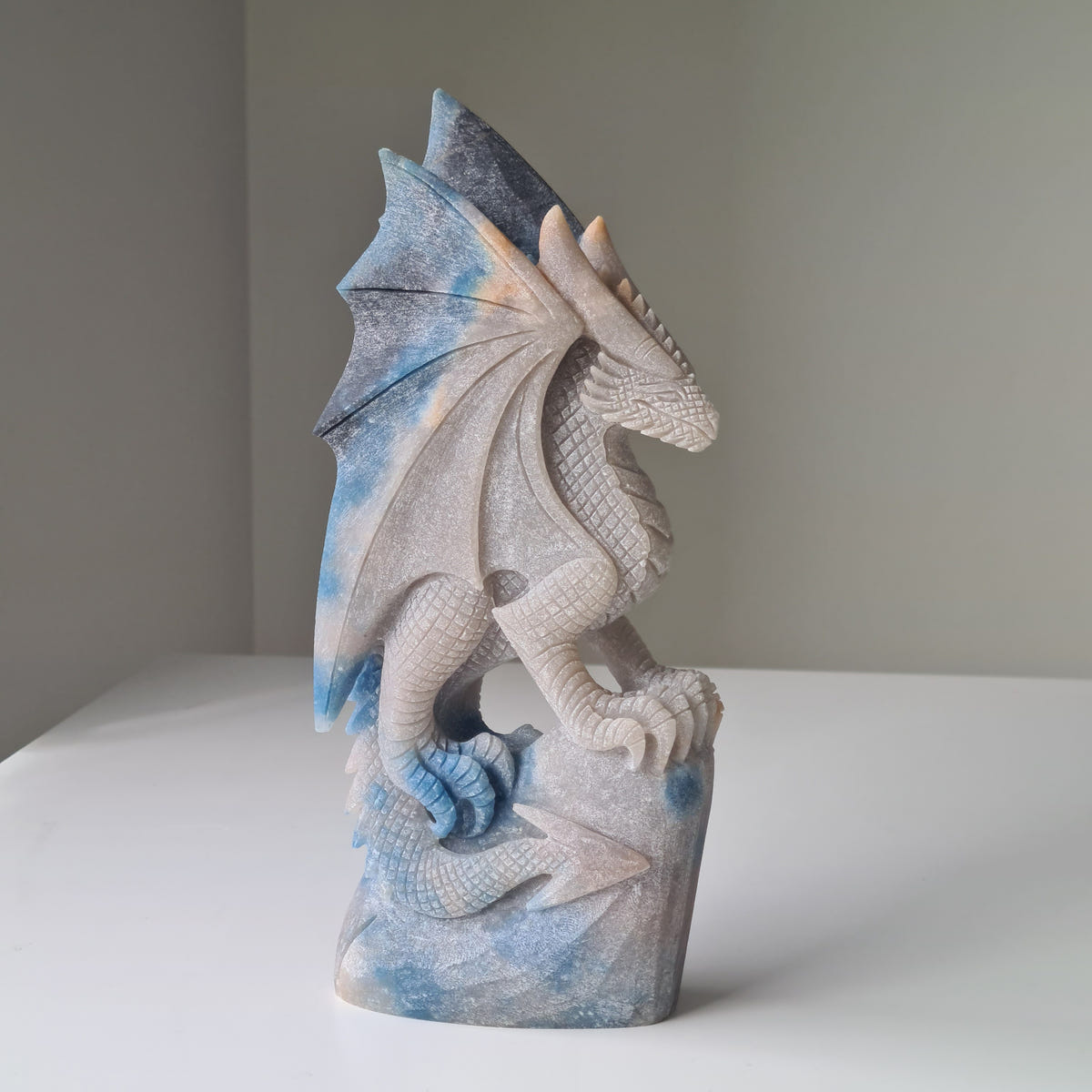 Upright trolleite dragon carving with raised wings and a curled tail in pale blue and cream stone.