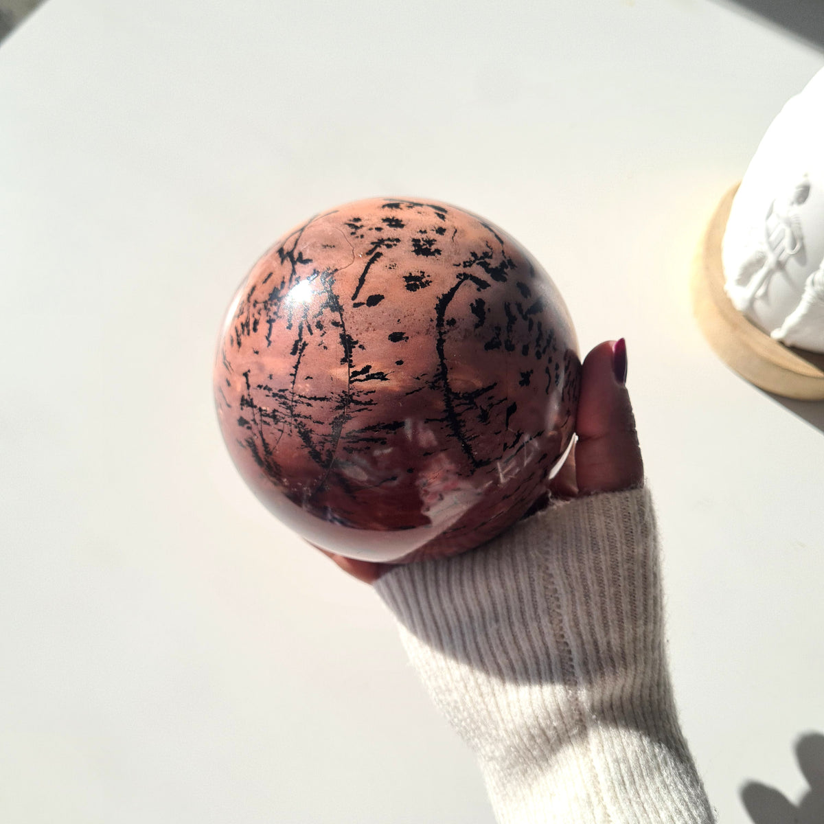 Hand-held picture jasper sphere with fine black streaks across peach and red areas.