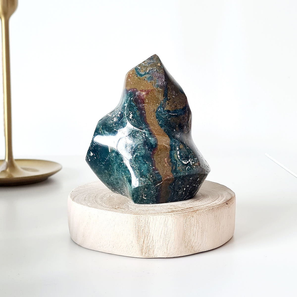 Ocean jasper flame C with deep green, white and ochre bands, displayed on a round wooden base.