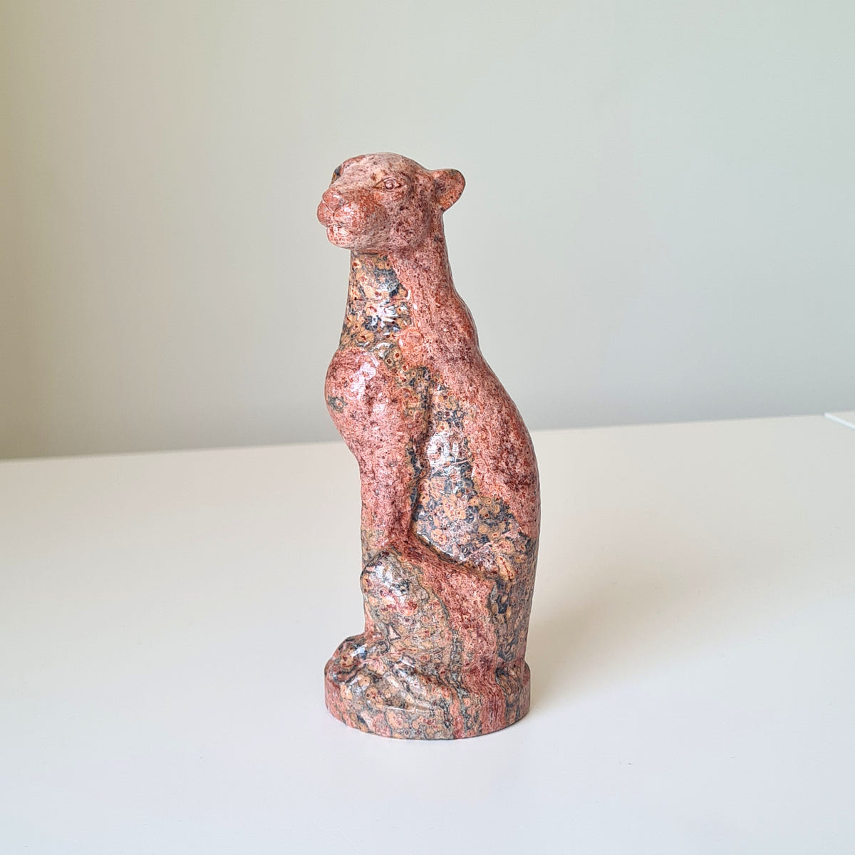 Jasper leopard carving D with warm pink and dark mineral patterns, seated upright on an oval base.